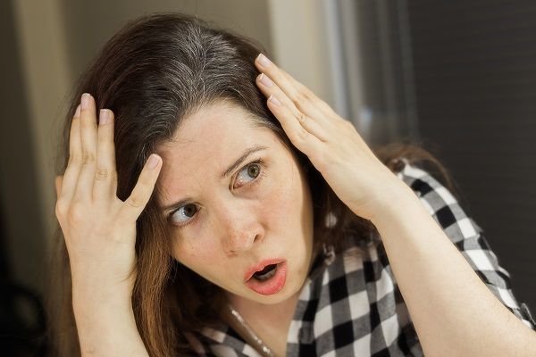 causas da caspa - Mulher olha, perplexa, para o couro cabeludo coberto de caspa