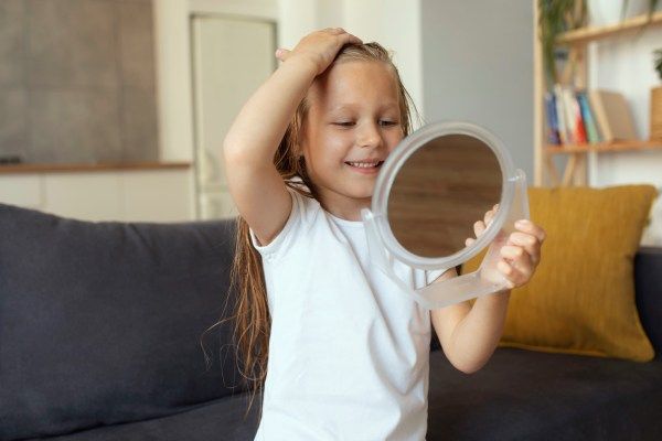 Menina verificando no espelho se ela tem alopecia - Alopecia em crianças 