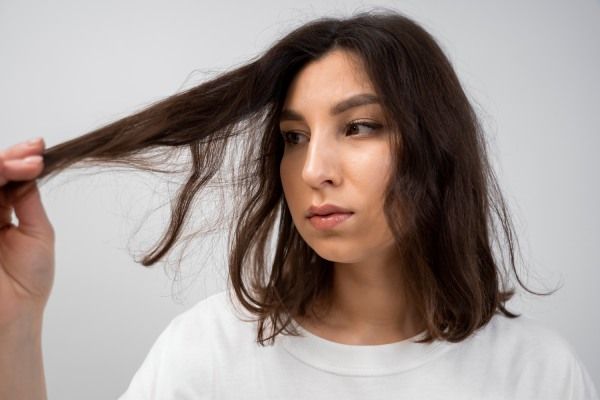 Mulher olhando detalhadamente seu cabelo para detectar se sofre de tricorrexis nodosa 