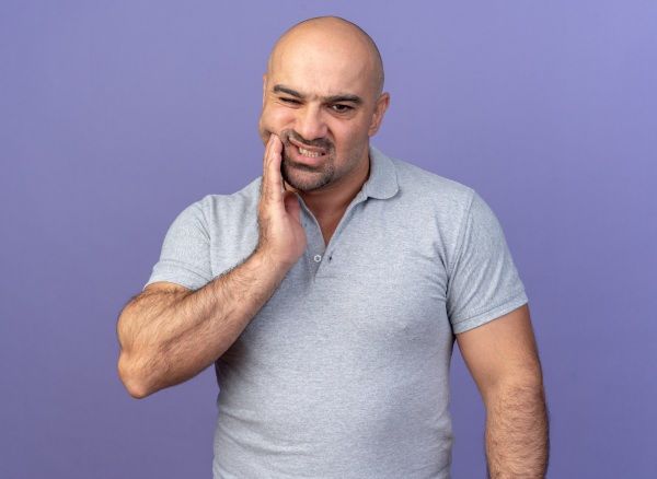 Homem com cárie e calvície dolorido, com a mão na bochecha
