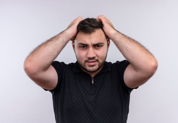 Jovem barbudo de camisa preta estressado e nervoso puxando o cabelo - transplante capilar malsucedido