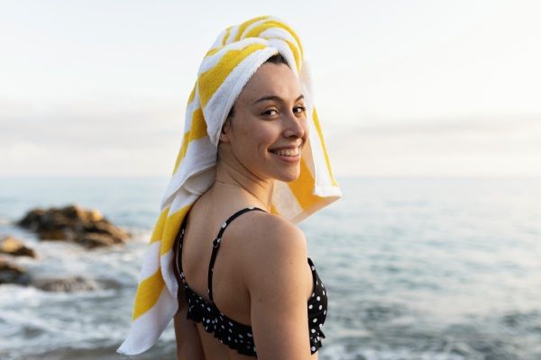 Mulher na praia secando o cabelo com uma toalha