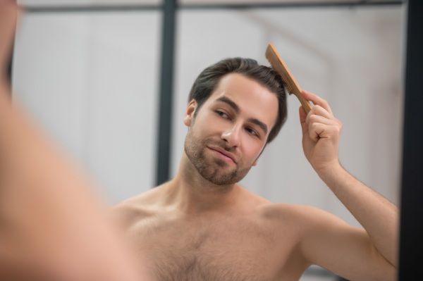 Estilo de cabelo. Jovem bonito escovando o cabelo e parecendo satisfeito