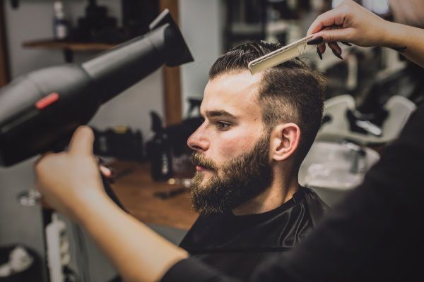 Cortar a mulher secando o cabelo do homem na barbearia - cortar o cabelo após um transplante capilar