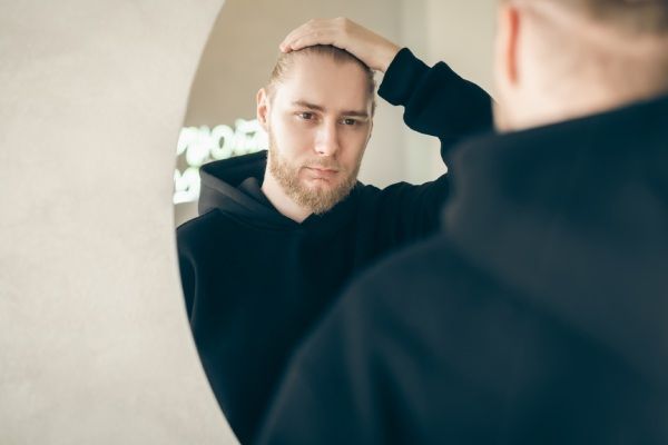 Um jovem atraente com barba se olha no espelho