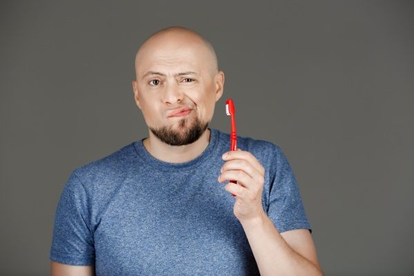 Homem com cárie e calvície segurando a escova de dentes 