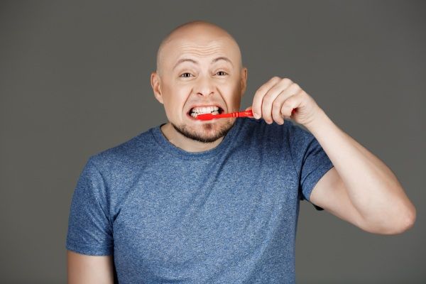 Retrato de homem bonito engraçado na camisa cinza, escovar os dentes ao longo da parede escura