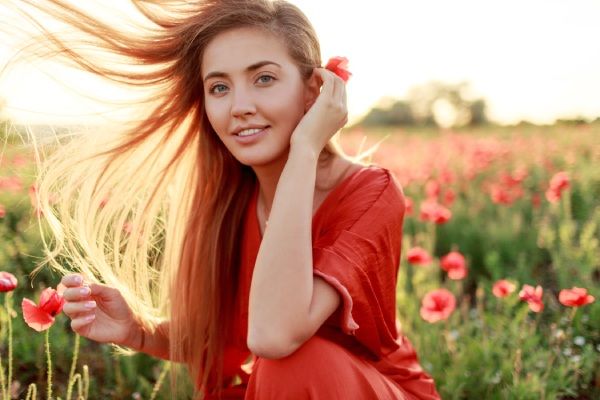 Una mujer rubia elegante se envuelve sobre su hombro y mira. Cabello ventoso. Pintoresco campo de amapolas en cálidos colores del atardecer.