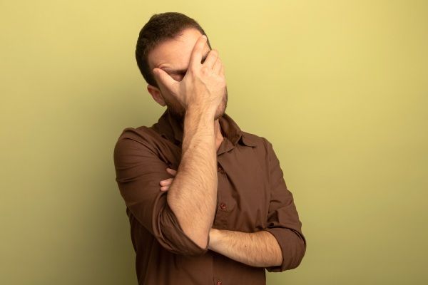 saúde mental masculina - Cansado jovem caucasiano cobrindo o rosto com a mão com os olhos fechados, isolado em um fundo verde oliva com espaço de cópia