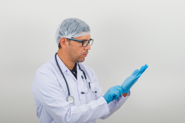 cirurgião de transplante capilar - Cirurgião masculino calçando luvas em jaleco branco