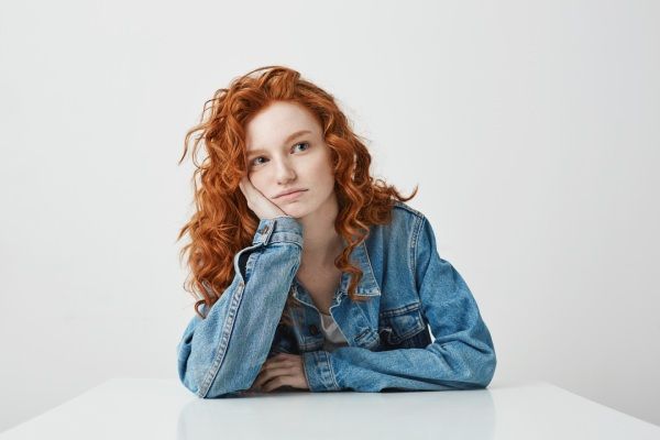 Menina bonita sonhadora que pensa sonhando sentado à mesa.