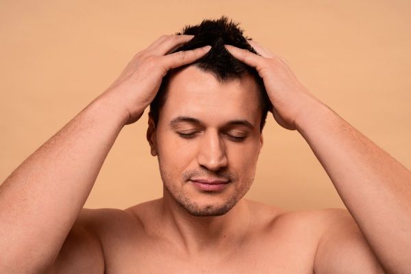 Homem de tiro médio a dar-se uma massagem no couro cabeludo