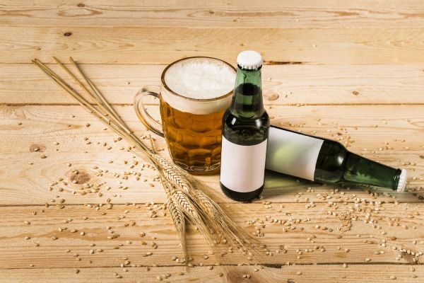 Copo de cerveja com garrafas e espigas de trigo na prancha de madeira