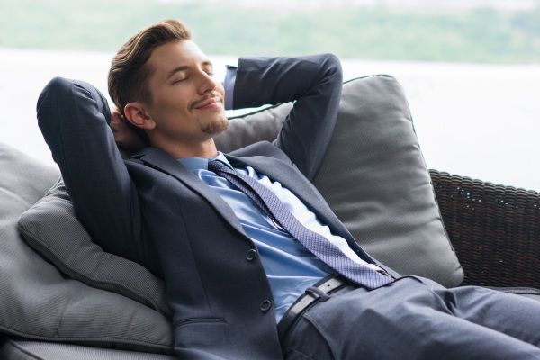 Homem de sorriso com mãos atrás da cabeça Dozing no sofá