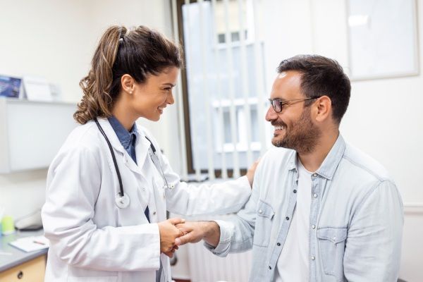 Médico jovem ou GP em uniforme médico branco consulta paciente do sexo masculino em hospital privado