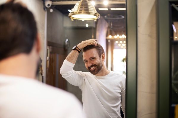 Homem feliz vendo os resultados do implante capilar no espelho