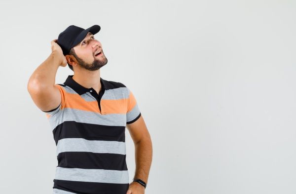 Jovem em t-shirt, boné, olhando para cima com a mão na cabeça e parecendo um sonho, vista frontal - Alopecia