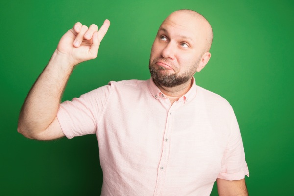 Impressionado ao olhar para o lado de um homem careca de meia-idade vestindo uma camiseta rosa apontando para cima isolado no verde