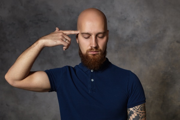 Conceito de tédio, fadiga e depressão. Foto isolada de homem caucasiano infeliz deprimido com barba espessa, segurando o dedo da frente na têmpora e fechando os olhos como se estivesse atirando, sentindo-se estressado