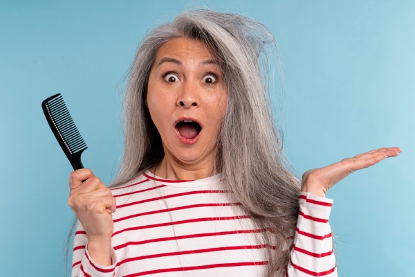Mulher sênior com cabelo emaranhado sendo surpreendida contra um fundo azul