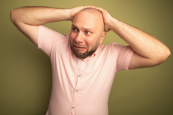 Preocupado em olhar para o lado de um homem careca de meia-idade usando uma camiseta rosa de mãos dadas atrás da cabeça