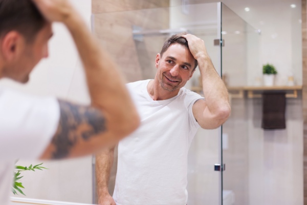 Homem feliz verificando o resultado de seu transplante de cabelo no espelho