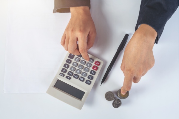 quanto custa um implante capilar - homem fazendo contas com uma calculadora e moedas