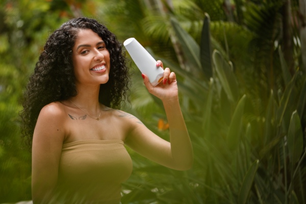 Cuidar do cabelo no verão - mulher posa com um condicionador na mão