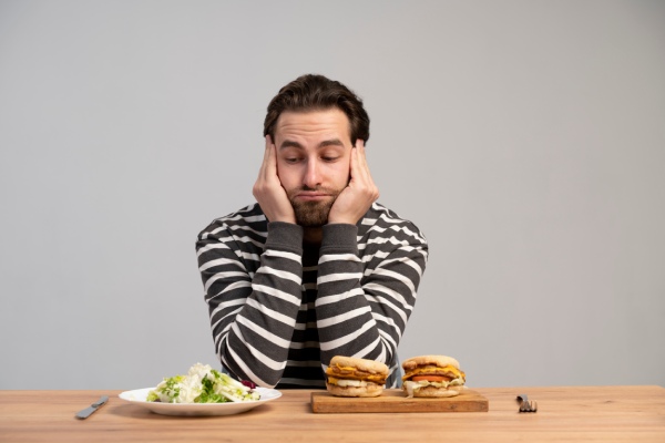 Homem ponderando tristemente se deve escolher alimentos saudáveis ou junk food