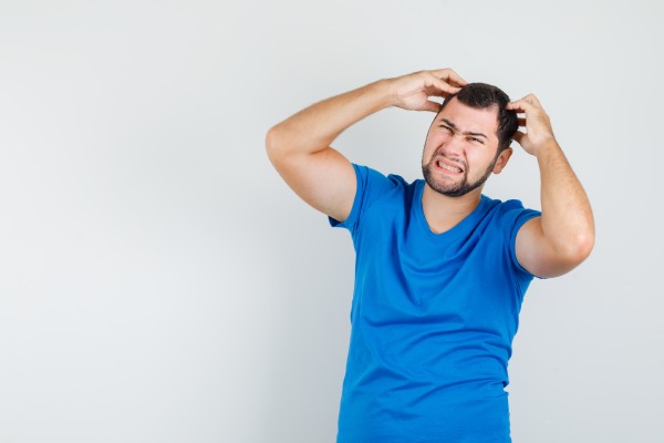 saúde mental masculina - Jovem homem segurando os dedos na cabeça, vestindo camiseta azul e parecendo irritado