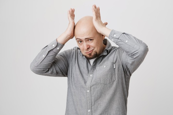 calvície - Um homem careca leva as mãos à cabeça, preocupado