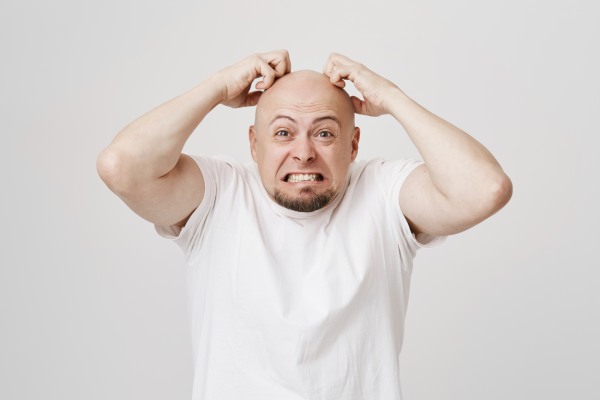 Menino careca e irritado range os dentes e coça a cabeça